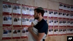 A man holds his baby as he looks at posters of the men, women and children held hostage by Hamas in the Gaza Strip, during a vigil marking 30 days since the October 7 Hamas attack that started the fighting, in Jerusalem, Nov. 5, 2023.