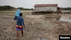 A man carries a bottle of water in a dry area of the Igarape do Taruma stream which flows into the Rio Negro River, in Manaus, Brazil, Oct. 16, 2023. 