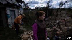 Artem Yarema, 13, chops wood, while his mother Tetiana Yarema, 48 stands in front of the family's house in Moshchun, near Kyiv, Ukraine, Oct. 10, 2023. Many Ukrainians have spent months preparing, including collecting firewood and buying generators.