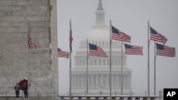 Visitors stand at the base of the Washington Monument as the dome of the Capitol is seen in the distance, in Washington, March 5, 2024.