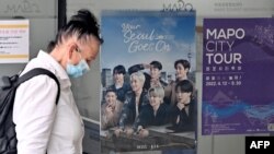 FILE - A woman walks past a poster featuring members of the K-pop group BTS, at a tourist information center in Seoul, South Korea, June 15, 2022.