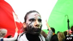 A protester wearing face-paint depicting France's iconic "Marianne" leading an uprising, stands under a giant Iranian flag as people gather in support of Kurdish woman Mahsa Amini during a protest, Oct. 2, 2022 on Place de la Republique in Paris, followin