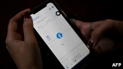 FILE - A woman checks Facebook on her mobile phone in Yangon, Feb. 4, 2021, as Myanmar's generals ordered internet providers to restrict access to Facebook, days after they seized power.