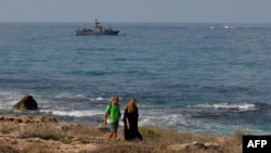 People walk along the beach as an Israeli navy vessel patrols the Mediterranean waters off Rosh Hanikra, known in Lebanon as Ras al-Naqura, on the Israeli side of the border between the two countries, on Oct. 7, 2022.