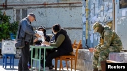 Seorang penduduk setempat menerima surat suara dari anggota komisi pemilihan sebelum memberikan suaranya ke dalam kotak suara pada hari ketiga referendum tentang bergabungnya Republik Rakyat Donetsk ke Rusia, di Ukraina, September 25, 2022. (Foto: REUTERS/Alexander Ermochenko)