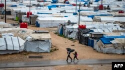 FILE - People use umbrellas as they walk in the rain at Camp Roj, where relatives of people suspected of belonging to the Islamic State (IS) group are held, in the countryside near al-Malikiyah (Derik) in Syria's northeastern Hasakah province, on March 4,