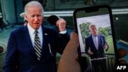 In this photo illustration created July 21, 2022, in Washington, a video tweet from U.S. President Joe Biden is seen on a cell phone, juxtaposed against a computer screen showing Biden in the background.