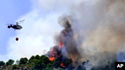 Un helicóptero lanza agua mientras un incendio forestal avanza cerca de una zona residencial en Alhaurín de la Torre, Málaga, España, el sábado 16 de julio de 2022. (AP Foto/Gregorio Marrero)