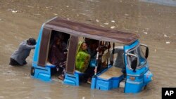 A rickshaw driver and a volunteer push a rickshaw stuck in a flooded road after a heavy rainfall in Karachi, Pakistan, July 11, 2022.