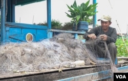 Sout To cleans up the gill nets in front of his floating house in Peam Bang village of Kampong Thom province, on May 04, 2022. (Khan Sokummono/VOA Khmer)