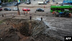 Municipal service workers stand near a crater near the damaged headquarters of the Kharkiv administration building following an overnight missile strike in Kharkiv, Aug. 29, 2022, amid Russia's military invasion launched on Ukraine.