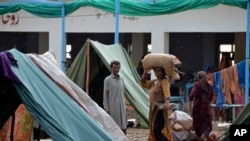 A displaced woman carries belongings in a light rain after fleeing her flood-hit homes in Sohbat Pur city, a district of Pakistan's southwestern Baluchistan province, Aug. 30, 2022.