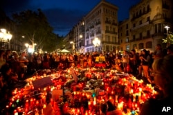 People gather at a memorial tribute of flowers, messages and candles to the victims on Barcelona's historic Las Ramblas promenade on the Joan Miro mosaic, embedded in the pavement where the van stopped after killing at least 13 people in Barcelona , Spain.