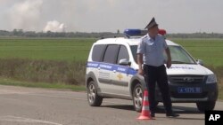In this image taken from video provided by the RU-RTR Russian television on Aug. 16, 2022, a policeman blocks a way to the site of explosion at an ammunition storage of Russian army near the village of Mayskoye, Crimea.