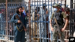 FILE - A Pakistani paramilitary soldier, right, and a Taliban fighter stand guard on their respective sides at a border crossing point between Pakistan and Afghanistan, in Torkham, in the Khyber district of Pakistan, Aug. 21, 2021. 
