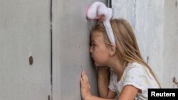 A child named Anhelina looks through a shrapnel hole in a fence after a recent Russian military strike on the southern Ukrainian city of Mykolaiv, August 10, 2022. 