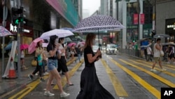 People wearing face masks, walk in the rain in Hong Kong, Tuesday, Aug. 9, 2022. 