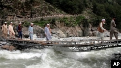 People cross a river on a bridge damaged by floodwaters, in the town of Bahrain, Pakistan, Aug. 30, 2022.
