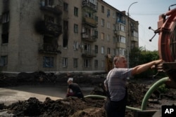 Workers drain water from a crater created by an explosion that damaged a residential building after a Russian attack in Slovyansk, Ukraine, Sunday, Aug. 28, 2022.