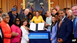 House Speaker Nancy Pelosi of Calif., surrounded by House Democrats, stands up after signing the Inflation Reduction Act of 2022 during a bill enrollment ceremony on Capitol Hill in Washington, Aug. 12, 2022.