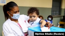 Une femme vote avec son bébé à l'école Nzinga Mbandi à Luanda, en Angola, le 24 août 2022. 