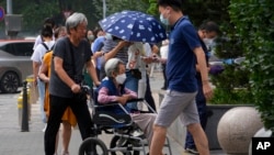 FILE - A man pushes an elderly woman in a wheelchair in Beijing, July 5, 2022.