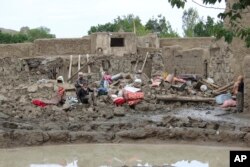 People collect their belongings from their damaged homes after heavy flooding in the Khushi district of Logar province south of Kabul, Afghanistan, Sunday, Aug. 21, 2022.