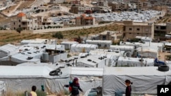 FILE - Syrian refugee children play at an informal refugee camp, which is seen set between the houses and buildings in Arsal, near the border with Syria, east Lebanon, June 13, 2018.