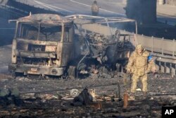 A Ukrainian soldier walks past debris of a burning military truck, on a street in Kyiv, Ukraine, Feb. 26, 2022.