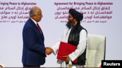 FILE -Mullah Abdul Ghani Baradar, the leader of the Taliban delegation, and Zalmay Khalilzad, U.S. envoy for peace in Afghanistan, shake hands after signing an agreement between members of Afghanistan's Taliban and the U.S., in Doha, Qatar, Feb. 29, 2020.