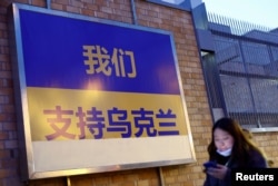 Seorang perempuan berjalan melewati papan reklame yang mendukung Ukraina setelah invasi Rusia ke negara itu, di Beijing, China, 2 Maret 2022. (Foto: Reuters)