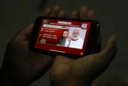 A man in Hyderabad, India watches on his mobile phone Prime Minister Narendra Modi address the nation in a televised speech about COVID-19 situation, April 14, 2020.