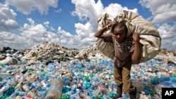FILE - A man walks on a mountain of plastic bottles as he carries a sack of them to be sold for recycling after weighing them at the dump in the Dandora slum of Nairobi, Kenya, on Dec. 5, 2018. 