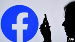 FILE - In this photo illustration, a person looks at a smartphone with a Facebook App logo displayed on the background, in Arlington, Va., Aug. 17, 2021. 