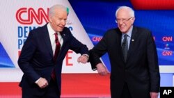 Bivši potpredsjednik SAD Džozef Bajden i senator iz Vermonta Berni Sanders pozdravljaju se laktovima pred početak debate u studiju kablovske mreže CNN u Vašingtonu u nedjelju 15. marta 2020. (Foto: AP/Evan Vucci)
