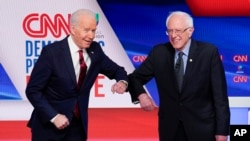 Mantan wakil presiden AS Joe Biden (kiri) dan Senator Bernie Sanders (kanan) saling menyapa sebelum debat Pilpres 2020 di Studio CNN di Washington, Minggu, 15 Maret 2020. (Foto: AP)