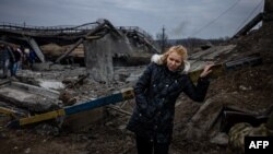 A woman rests after crossing a destroyed bridge as she evacuates from the city of Irpin, northwest of Kyiv, on March 7, 2022.