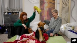 Olga Okhrimenko, right, 34 years-old, who fled the Russian invasion from Kharkiv on March 1, plays her dog Knolly as they sit inside a ballroom converted into a makeshift refugee shelter, in Suceava, Romania, Friday, March 4, 2022. (AP Photo/Andreea Alexandru)