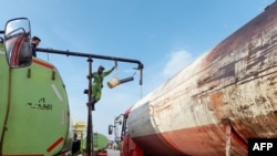 Para petugas memindahkan minyak sawit mentah ke truk tangki di pelabuhan Tanjung Emas Semarang, sebelum didistribusikan ke pabrik pengemasan minyak goreng, 7 April 2022. (Daffa Ramya KANZUDDIN / AFP)