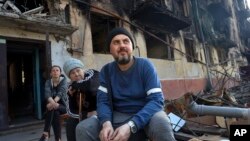 Local residents sit in front of a damaged apartment building from heavy fighting in an area controlled by Russian-backed separatist forces in Mariupol, Ukraine, April 26, 2022.
