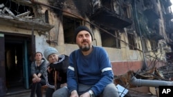 Los residentes locales se sientan frente a un edificio de apartamentos dañado por los intensos combates en un área controlada por las fuerzas separatistas respaldadas por Rusia en Mariúpol, Ucrania, el 26 de abril de 2022.