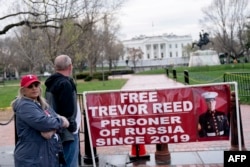 FILE - Paula and Joey Reed, parents of Trevor Reed, stand next to a banner reading "Free Trevor Reed" in Lafayette Square near the White House in Washington, March 30, 2022.