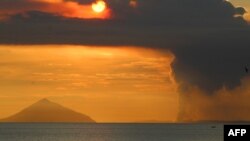 Matahari terbenam di balik Gunung Anak Krakatau (kanan) yang mengepulkan asap tebal, terlihat dari Pantai Pasauran, Anyer, Serang, 24 April 2022. (DZIKI OKTOMAULIYADI / AFP)