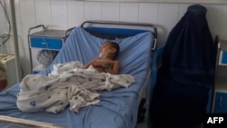 A burqa clad Afghan woman sits next to a child receiving treatment at a hospital after he got injured in a bomb blast in Kunduz on April 21, 2022.