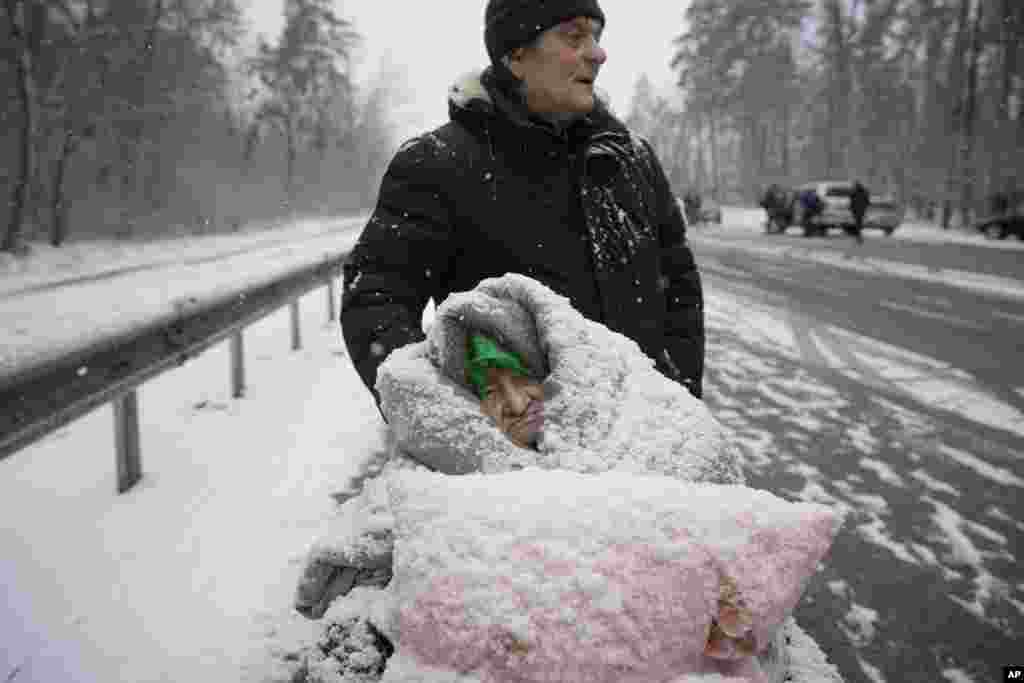 An elderly woman is coated in snow as she is evacuated in a wheelchair from Irpin, March 8, 2022.