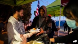 A migrant, center, receives a hot meal from volunteers outside the Sacred Heart Church in downtown El Paso, Texas, Jan. 7, 2023.