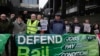 Mick Lynch, Sekjen Serikat Kereta Api, Maritim dan Transportasi (RMT) (jaket biru bertopi), bergabung dengan para pekerja kereta api Inggris selama aksi pemogokan di luar stasiun Euston di London. 