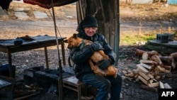 Anatoly Gysenko, 60, hugs a dog in the street outside his damaged home in the city of Lyman, Donetsk region, Ukraine, on Jan. 4, 2023. 