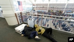 A pair of travelers sleep while fellow travelers queue up below to pass through the south security checkpoint in Denver International Airport Dec. 23, 2022, as a winter storm swept over the country.