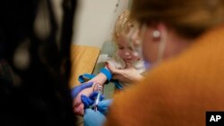 Alyssa Carpenter, 3, at her arm as research nurse Michelle Harris, left, and advanced practice nurse practitioner Lauren Arrigoni, right, draw blood at Children's National Hospital in Washington, Feb. 28, 2022.